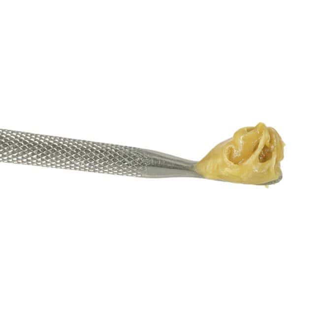 Close-up of beige cannabis concentrate on a metal dab tool against a white background.