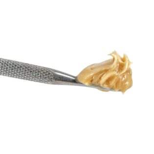Close-up of a metal dab tool holding a smooth, glossy beige cannabis concentrate against a crisp white background.