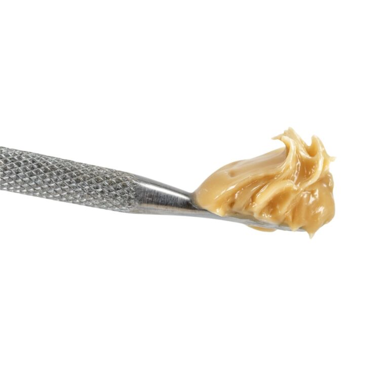 Close-up of a metal dab tool holding a smooth, glossy beige cannabis concentrate against a crisp white background.