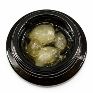 Close-up of cannabis concentrate diamonds in sauce inside a black extract jar on a white background