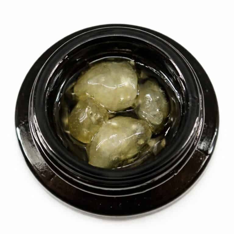 Close-up of cannabis concentrate diamonds in sauce inside a black extract jar on a white background