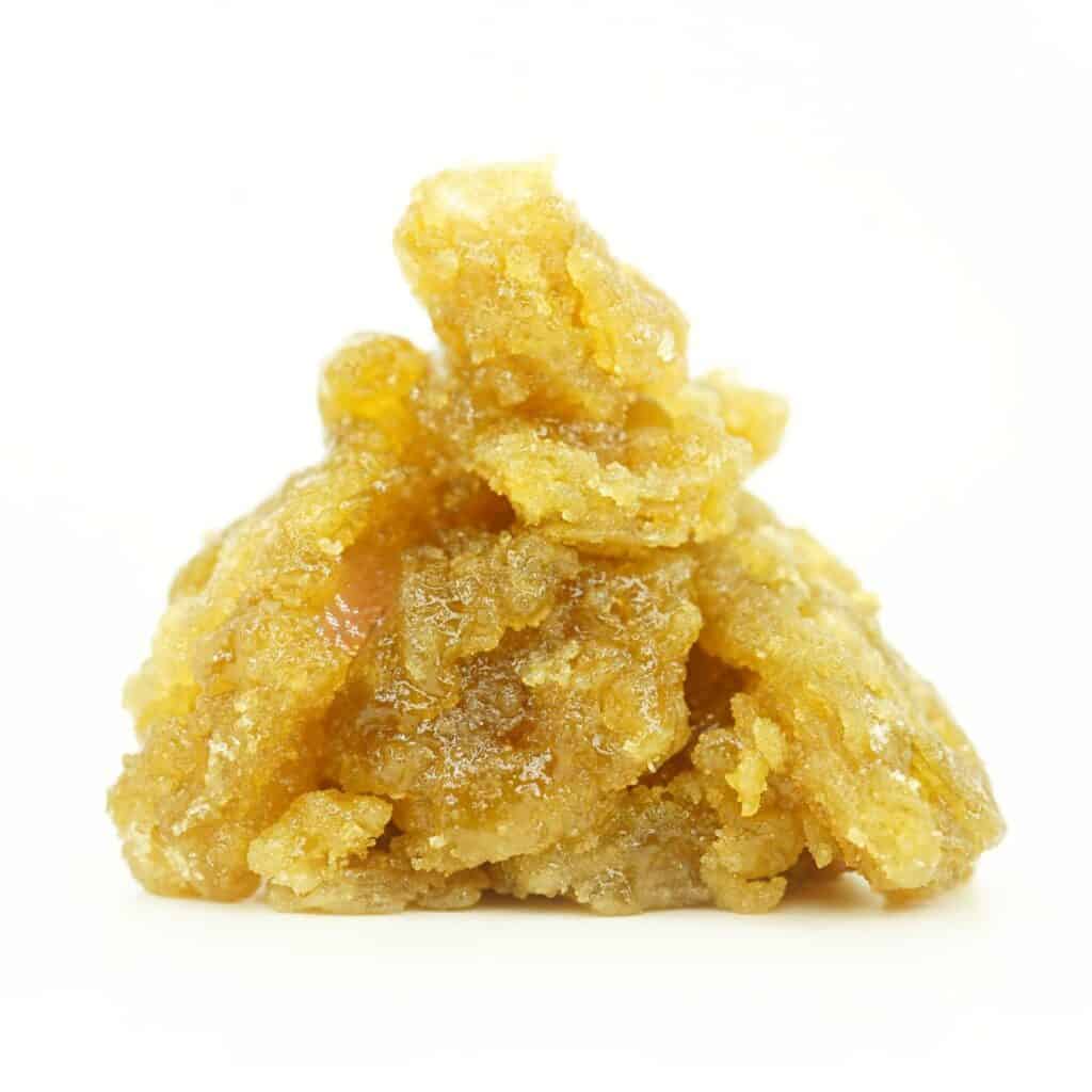 Close-up image of golden cannabis concentrate with a rich, glossy, and crystalline texture, piled in a small mound on a clean white background.