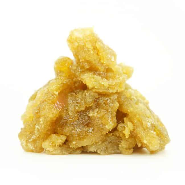 Close-up image of golden cannabis concentrate with a rich, glossy, and crystalline texture, piled in a small mound on a clean white background.