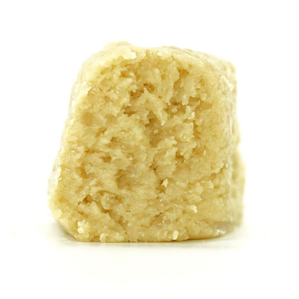 blue maui Close-up Pale yellow cannabis extract with a crumbly texture displayed upright on a white background