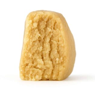 close-up of a light beige, crumbly concentrate piece displayed on a crisp white background, showing fine granular texture and natural depth with soft, even lighting.