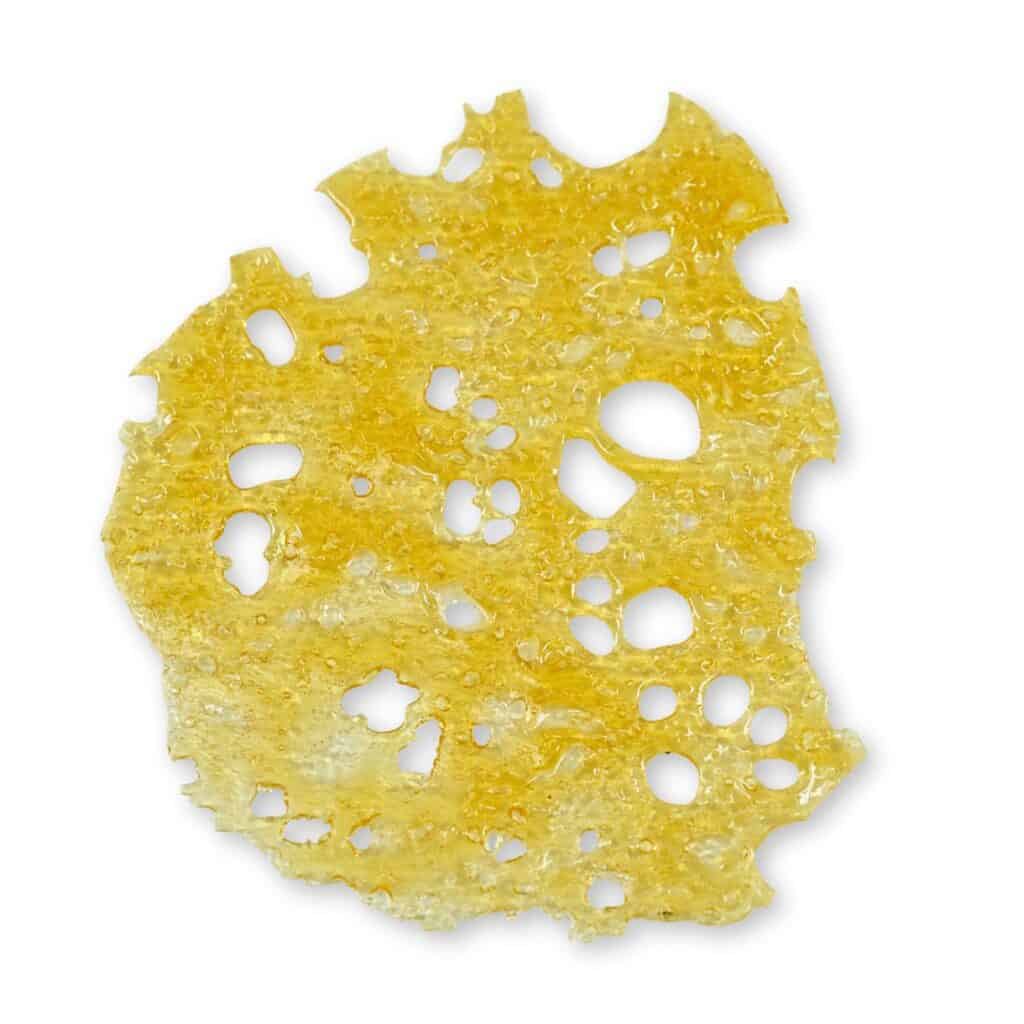 Close-up of golden cannabis shatter — thin, glassy sheet with bubbled and perforated texture on a clean white background.