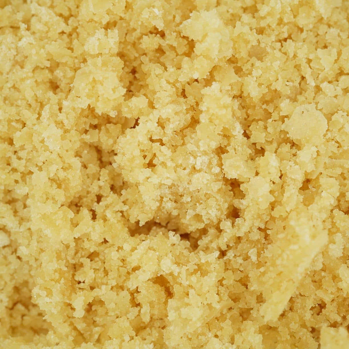 Sugar wax cannabis concentrate with golden, crumbly texture and granular consistency (close-up)