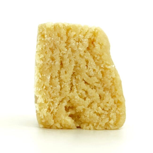 Pale yellow cannabis extract with a crumbly texture displayed upright on a white background