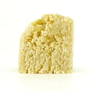 Close-up of a light yellow cannabis concentrate with a smooth, slightly crumbly texture on a white background.