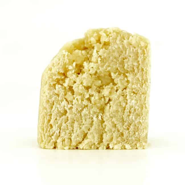 Close-up of a light yellow cannabis concentrate with a smooth, slightly crumbly texture on a white background.