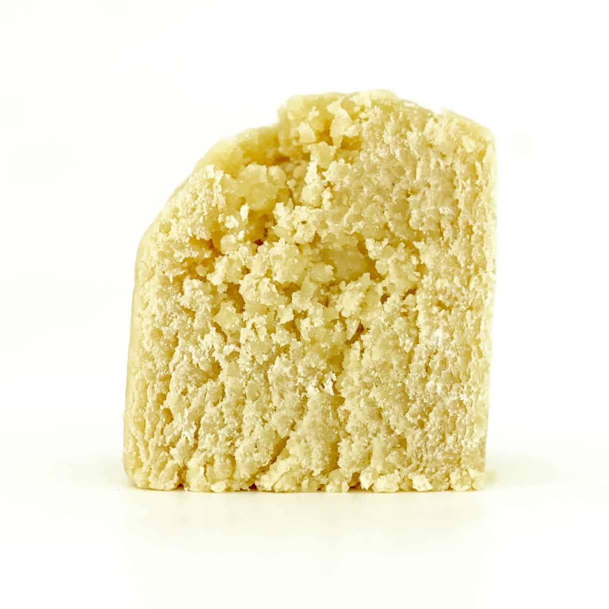 Close-up of a light yellow cannabis concentrate with a smooth, slightly crumbly texture on a white background.