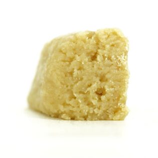Pale yellow cannabis extract with a crumbly texture displayed upright on a white background