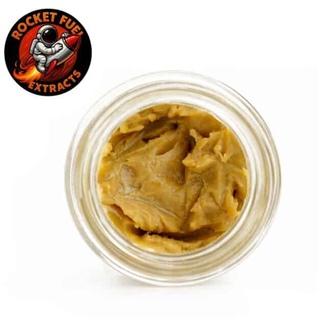 Open glass jar containing golden cannabis concentrate with smooth, creamy texture, photographed from above on a clean white background with rocket fuel logo