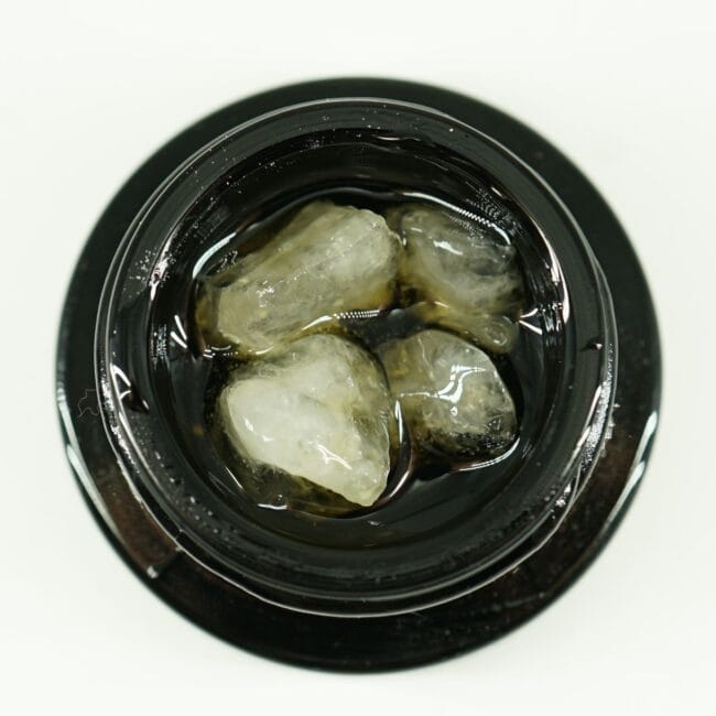 Close-up of cannabis concentrate diamonds in sauce inside a black extract jar on a white background