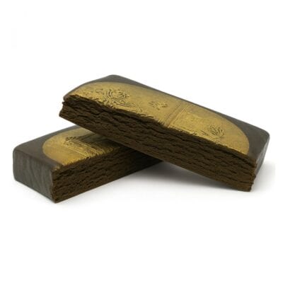 Two gold-stamped blocks of pressed hashish stacked on a white background, showcasing a smooth outer layer with embossed detailing and a crumbly interior texture.