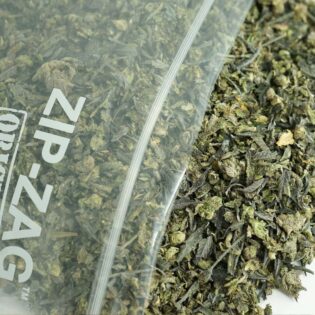 Cannabis trim in a Zip-Zag bag with dried shake, leaves, and stems on a white background.