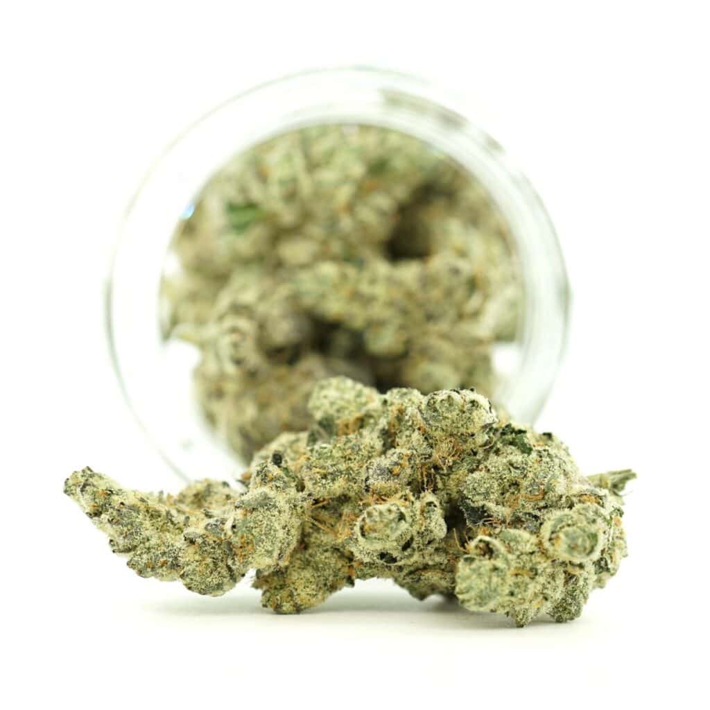Close-up of frosty cannabis buds spilling from a glass jar on a white background, showcasing dense trichomes and crystal-covered texture