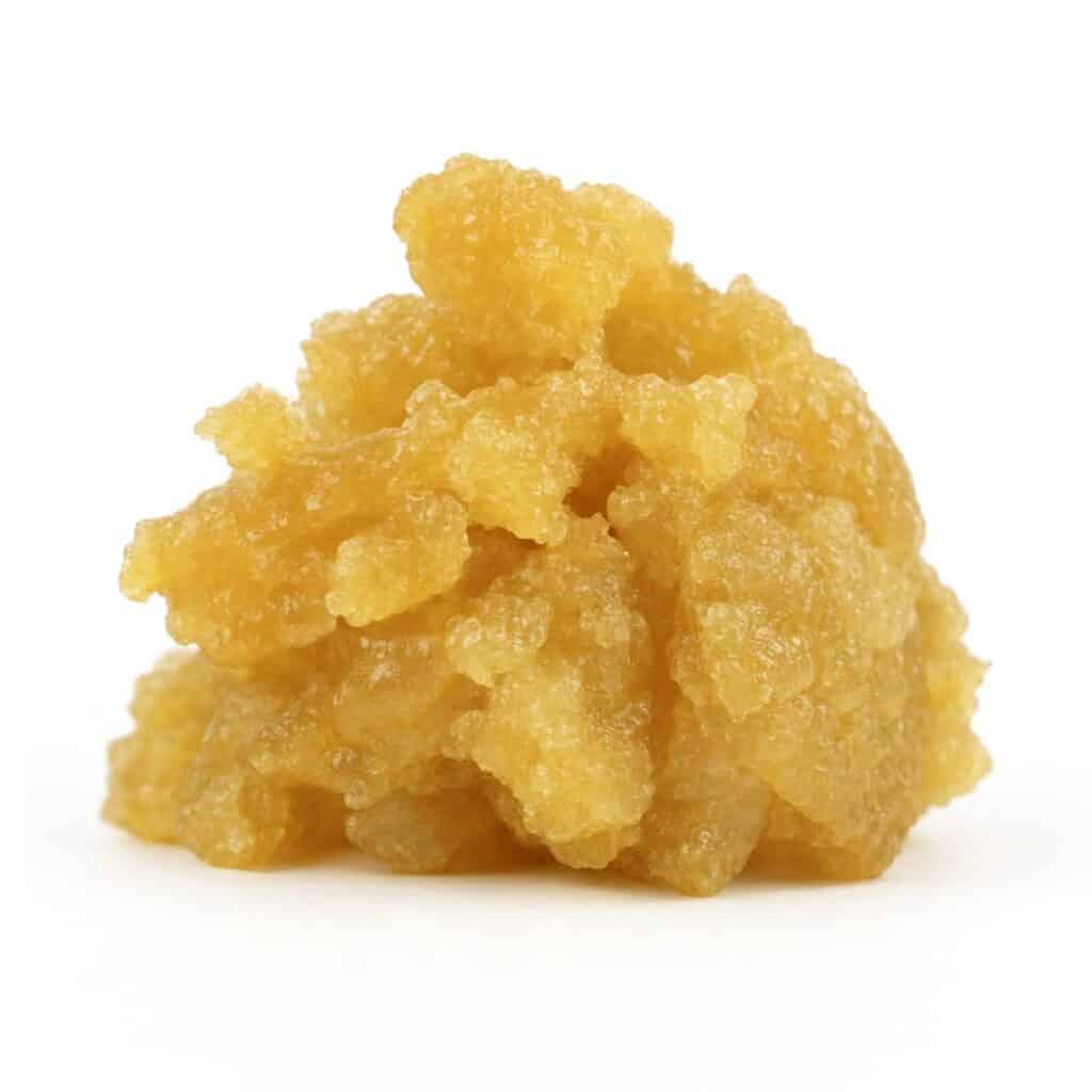 Golden cannabis concentrate with a moist, crystalline texture on a clean white background, showcasing its rich amber tones and granular structure
