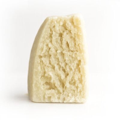 Photorealistic close-up of a wedge of aged crumbly cheese on a crisp white background for product display.