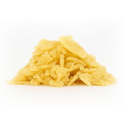 Pile of golden-yellow cannabis concentrate flakes on a crisp white background, photographed with sharp detail and balanced lighting.