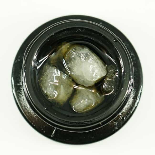 Close-up of cannabis concentrate diamonds in sauce inside a black extract jar on a white background