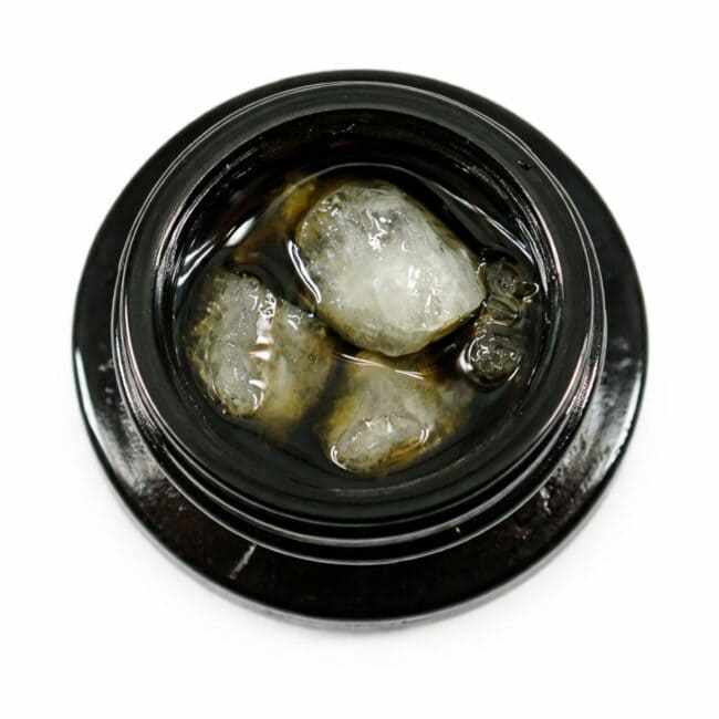 Close-up of cannabis concentrate diamonds in sauce inside a black extract jar on a white background