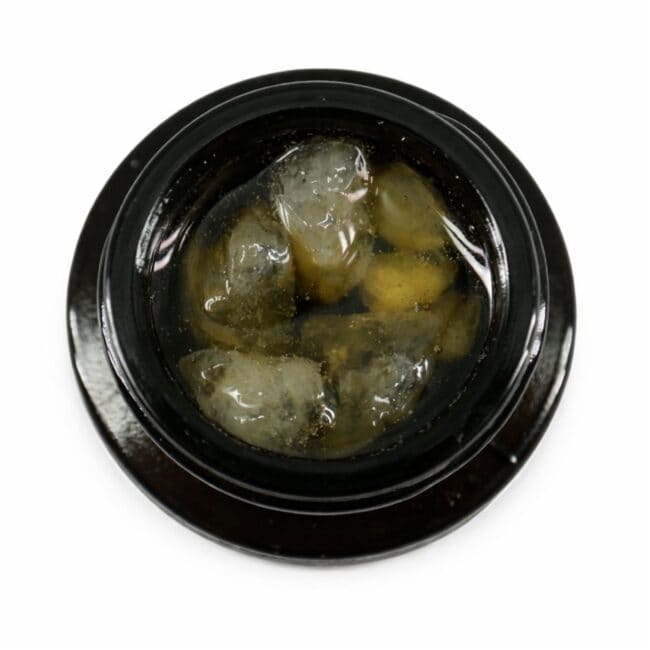 Close-up of cannabis concentrate diamonds in sauce inside a black extract jar on a white background
