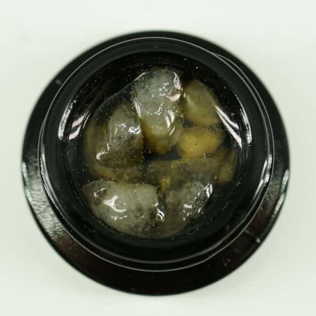 Close-up of cannabis concentrate diamonds in sauce inside a black extract jar on a white background