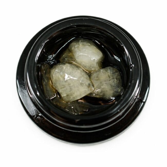 Close-up of cannabis concentrate diamonds in sauce inside a black extract jar on a white background