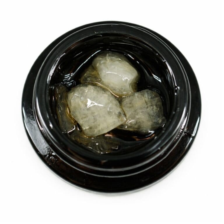 Close-up of cannabis concentrate diamonds in sauce inside a black extract jar on a white background