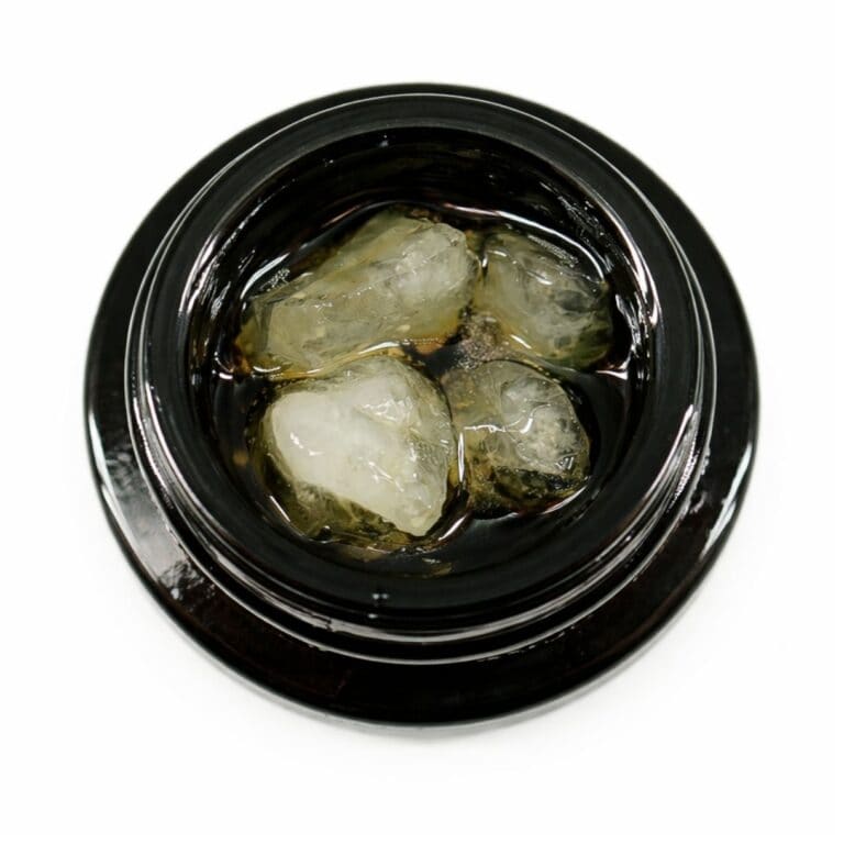 Close-up of cannabis concentrate diamonds in sauce inside a black extract jar on a white background