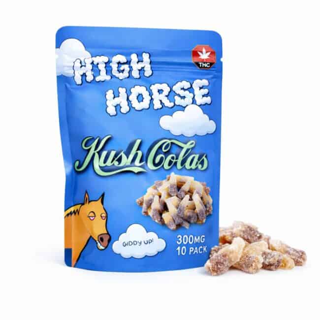 Blue resealable pouch of High Horse Kush Colas cannabis-infused cola bottle gummies with illustrated cloud graphics, THC symbol, and a pile of sugar-coated cola gummies displayed beside the package.