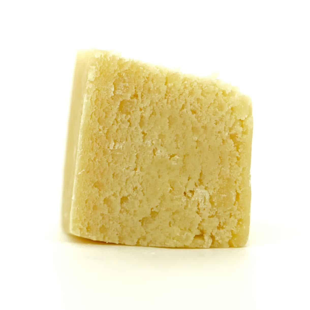 Close-up of a light yellow cannabis concentrate with a smooth, slightly crumbly texture on a white background.