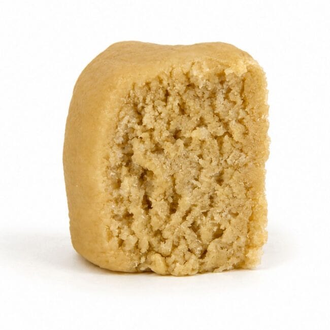 Premium light-golden cannabis concentrate with a smooth, dense texture, displayed as a sliced nug-style extract on a clean white background.