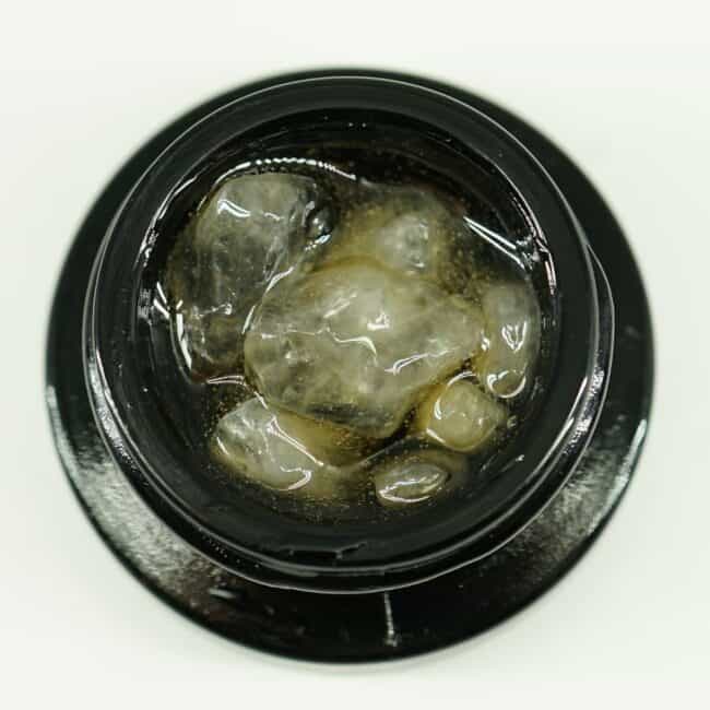Close-up of cannabis concentrate diamonds in sauce inside a black extract jar on a white background