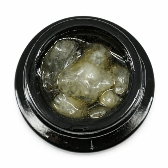 Close-up of cannabis concentrate diamonds in sauce inside a black extract jar on a white background