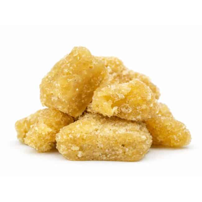Close-up of golden cannabis sugar concentrate crystals stacked on a crisp white background, showing granular texture and natural color variation.
