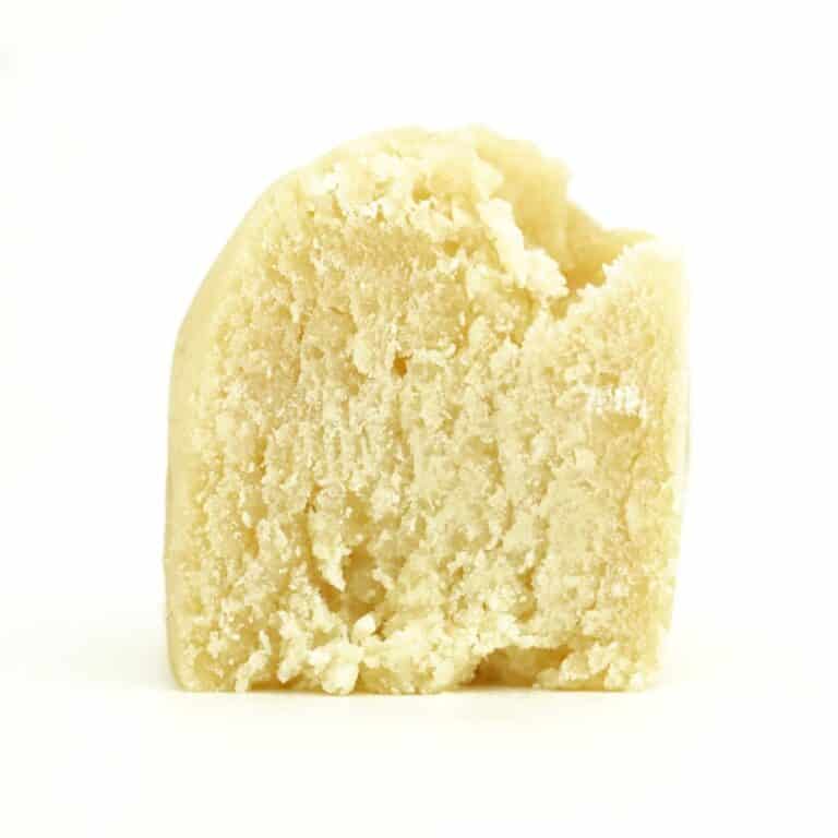 Close-up of a pale yellow cannabis concentrate with a soft, crumbly texture displayed on a white background.