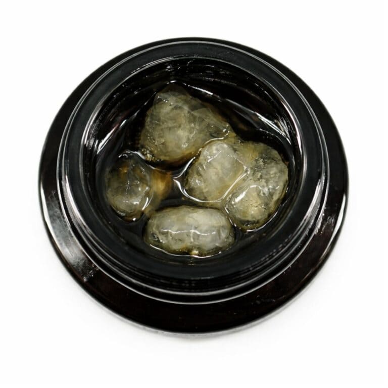 Close-up of cannabis concentrate diamonds in sauce inside a black extract jar on a white background
