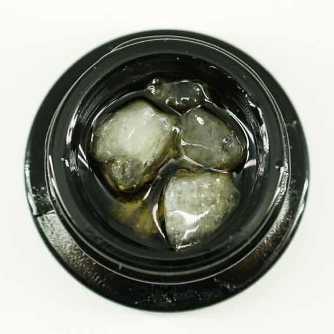 Close-up of cannabis concentrate diamonds in sauce inside a black extract jar on a white background
