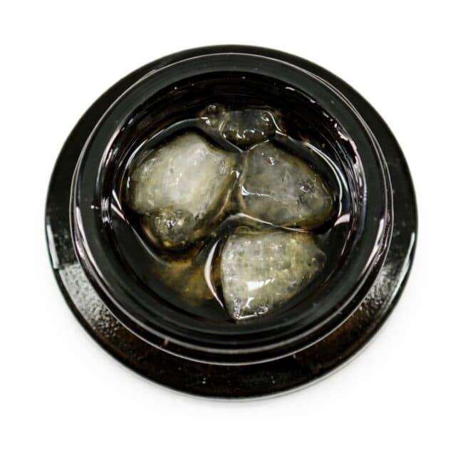 Close-up of cannabis concentrate diamonds in sauce inside a black extract jar on a white background