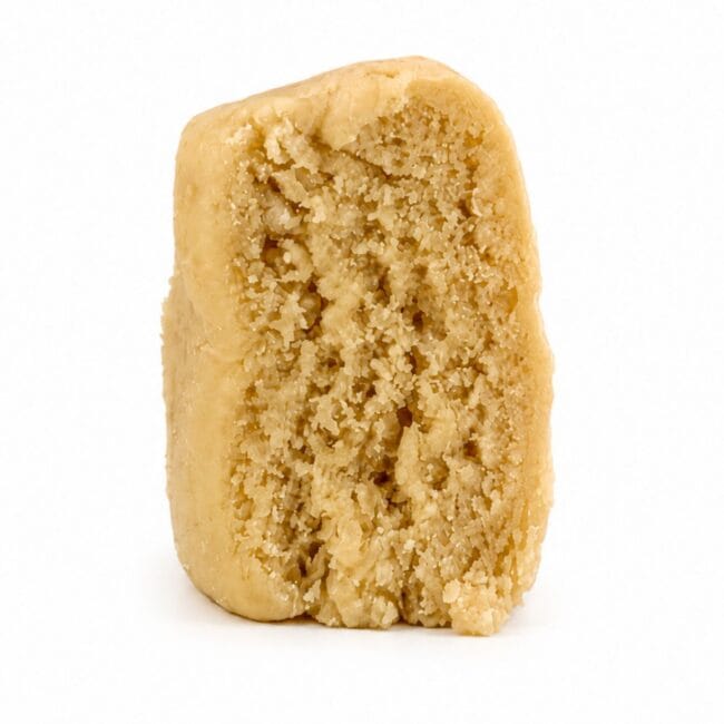 Premium light-golden cannabis concentrate with a smooth, dense texture, displayed as a sliced nug-style extract on a clean white background.