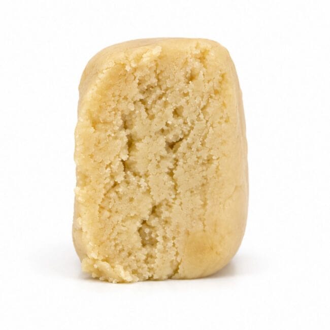 Premium light-golden cannabis concentrate with a smooth, dense texture, displayed as a sliced nug-style extract on a clean white background.