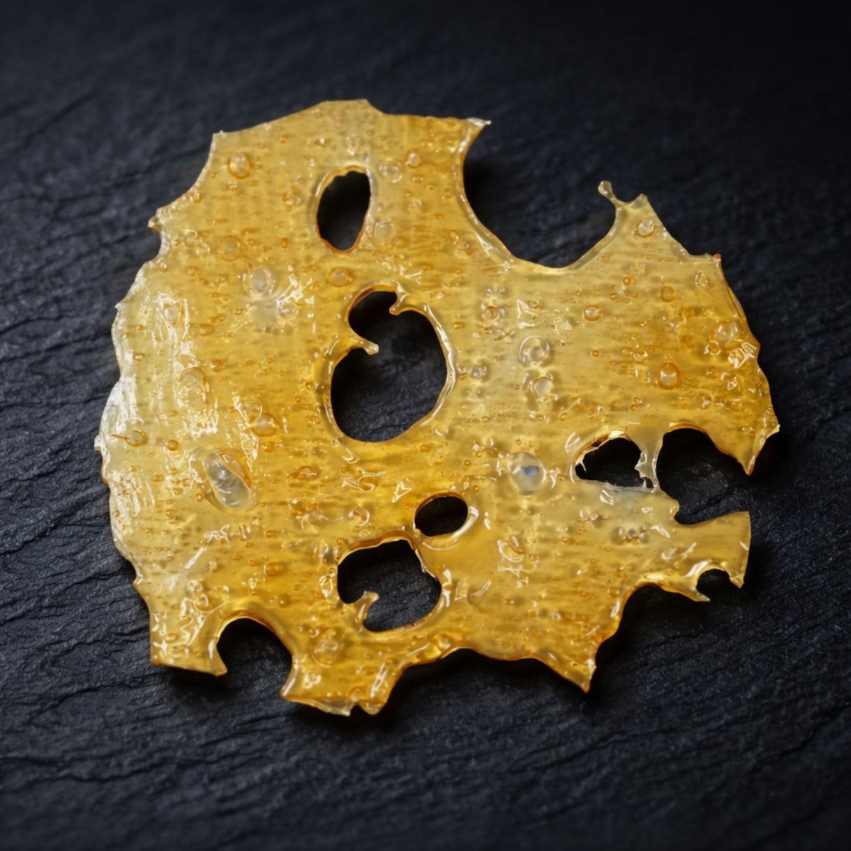 Close-up of a translucent golden cannabis concentrate slab with a porous, lace-like texture on a crisp white background. 