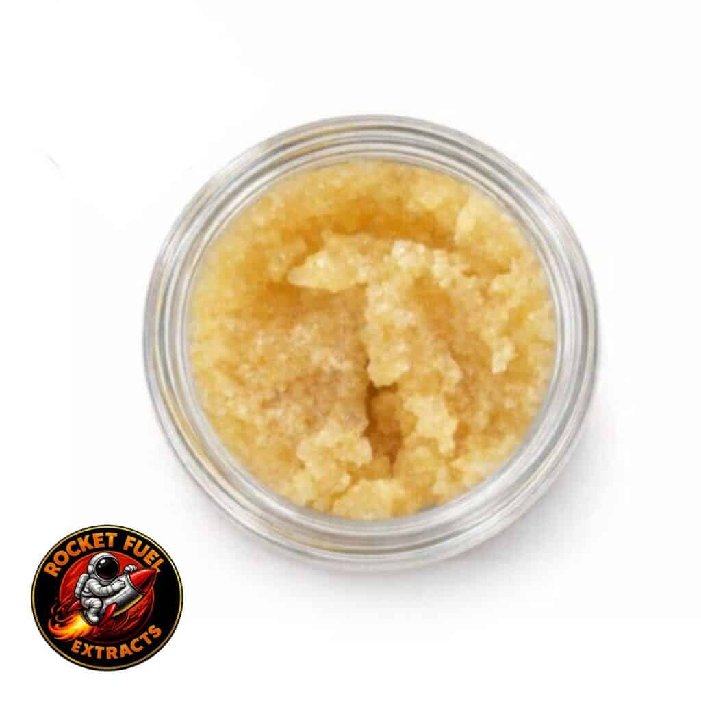 Open container of light-golden cannabis concentrate with a creamy, whipped texture on a white background.