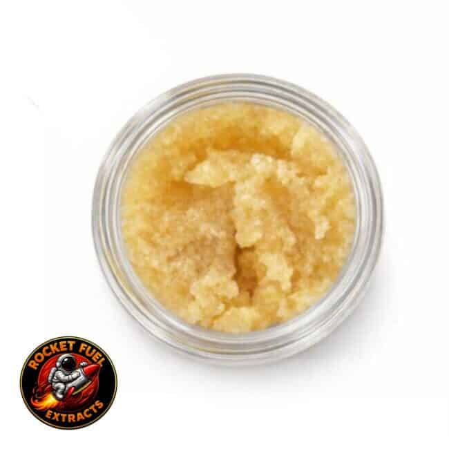 Open container of light-golden cannabis concentrate with a creamy, whipped texture on a white background.