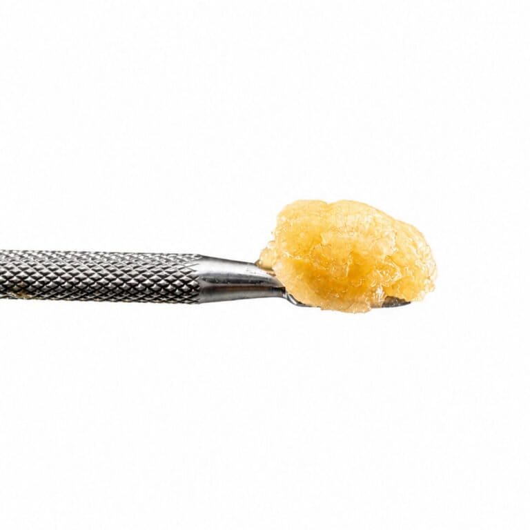 Ice Cream Cake Live Resin cannabis concentrate on a stainless steel dab tool with a golden terpene-rich extract against a white background.